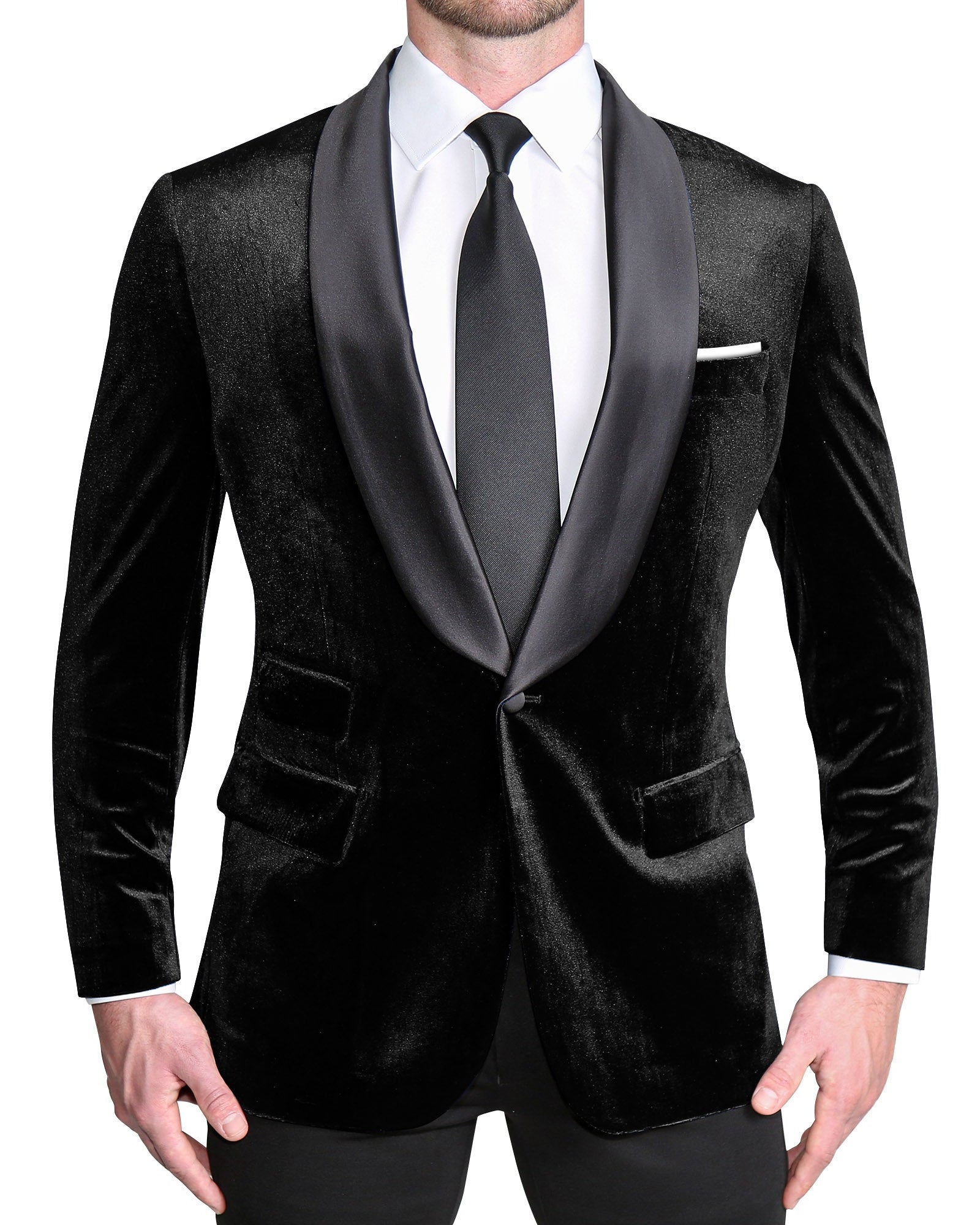 A male model wearing a black velvet tuxedo with a single-breasted jacket, shawl lapels, black satin buttons, and metal side-adjuster waistband.