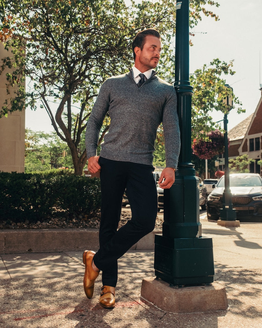 Man in a gray sweater and black pants standing on a sidewalk next to a streetlight.