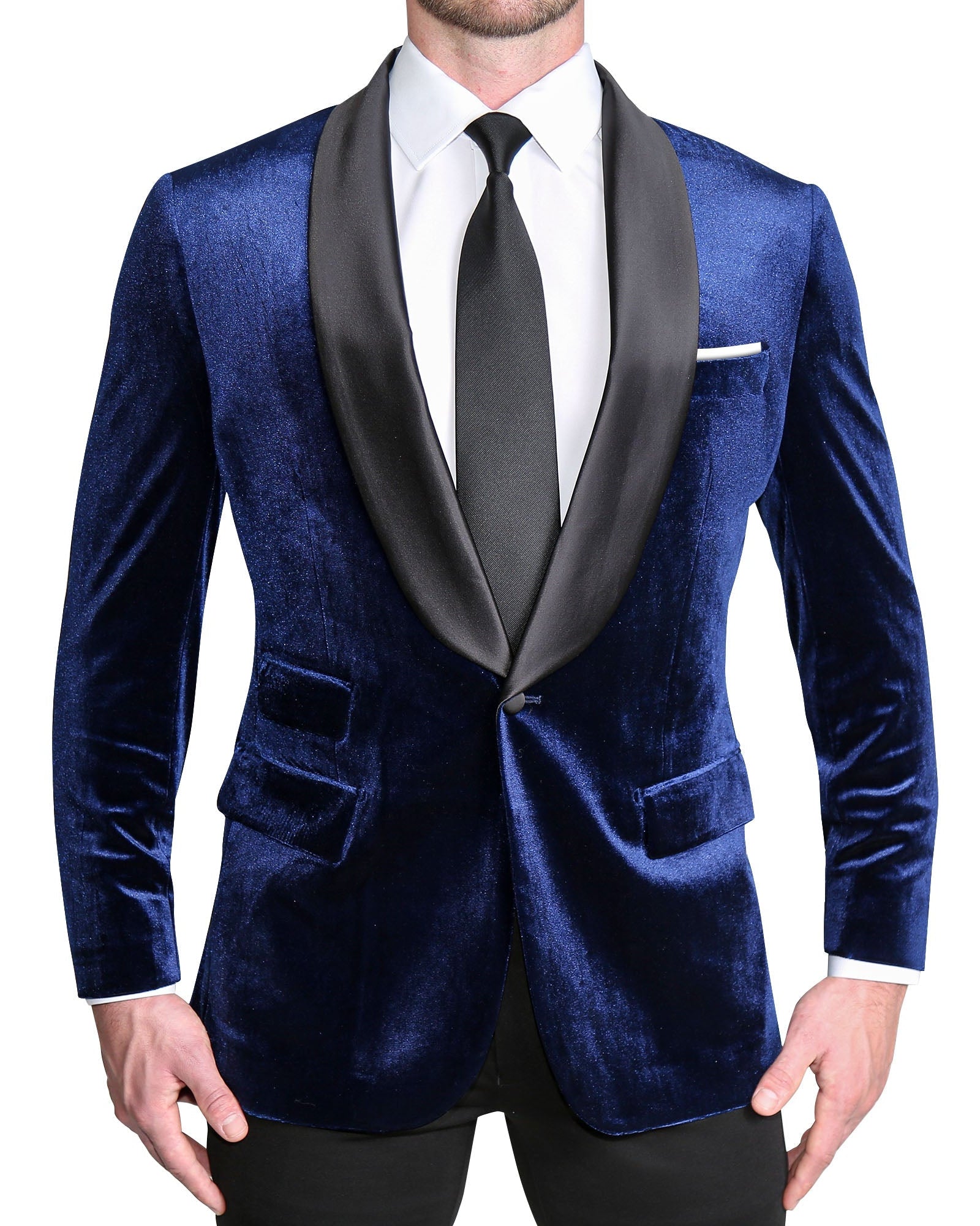 A man wearing a blue velvet tuxedo with shawl lapels, black satin buttons, and a white dress shirt. He is also wearing black trousers and a black tie.