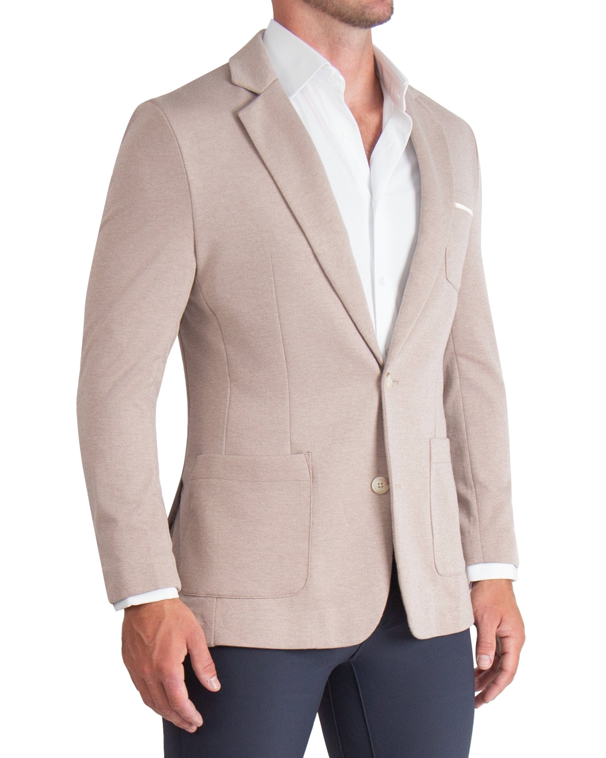A man wearing a athletic fit knit blazer in desert taupe with a white shirt and dark trousers. The blazer features two-button single-breasted design, medium notch lapels, patch pockets, and tortoise buttons.