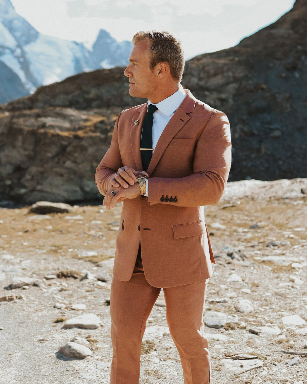 Man in a brown suit standing in a mountainous landscape